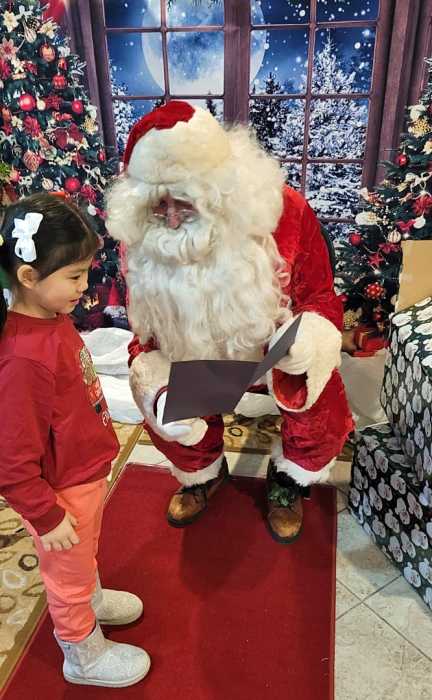 A little girl presents Santa Claus with a picture she drew and card she wrote for him.