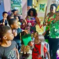President of the New Jersey-based Guyana Heritage Foundation Inc, Lady Ira Lewis flashes a big smile, as the happy kids looks on during a ribbon-cutting ceremony to unveil the Lady Ira Family Empowerment (LIFE) Library in the small Agricola Village, on the East Bank of Demerara in Guyana. The very first public reading room was launched on Jan. 10, 2026.
