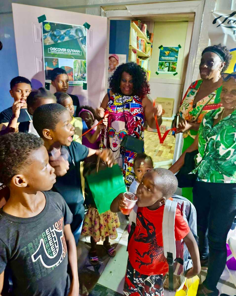 President of the New Jersey-based Guyana Heritage Foundation Inc, Lady Ira Lewis flashes a big smile, as the happy kids looks on during a ribbon-cutting ceremony to unveil the Lady Ira Family Empowerment (LIFE) Library in the small Agricola Village, on the East Bank of Demerara in Guyana. The very first public reading room was launched on Jan. 10, 2026.