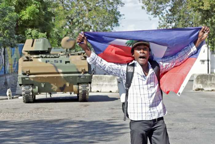 A man protests holding a Haitian flag while Haitian security forces guard the Prime Minister's office and the headquarters of the Transitional Presidential Council (CPT), as the mandate of the transitional governing council, formed to curb gang violence and pave the way for long-delayed election, is set to end on February 7 with no succession plan in place, in Port-au-Prince, Haiti, Feb. 6, 2026.
