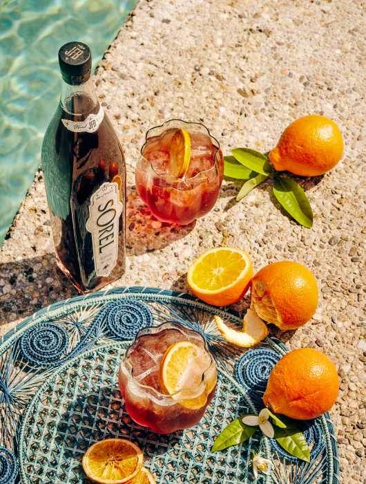 Bottles of Sorel Liqueur, made from hibiscus flowers and warming spices, are enjoyed poolside on a sunny day. The brand draws from Caribbean traditions passed down through generations.