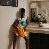 A photo of wearing heels, standing up against a wall with her right knee bent, and her right arm hanging off of a ledge.