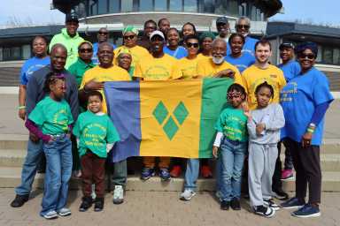 Walkathon participants, with Consul General Roland "Patel" Matthews, holding SVG national flag, second from left, in front of the pavilion at Marine Park in Brooklyn.