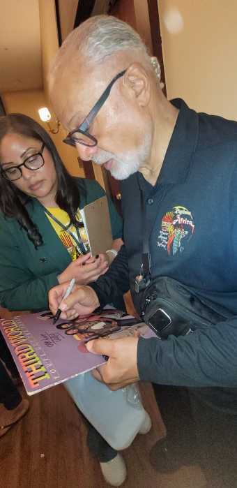 Wille Stewart, former drummer of Third World band and Rhythms of Africa concert curator backstage, signing Third World's iconic album jacket 'You've Got The Power' that was released in 1982 for a fan. Looking on is his daughter Akelia Stewart.