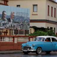 A vintage car passes by images of late Cuban President Fidel Castro, Cuba's former President Raul Castro, and Cuba's President Miguel Diaz-Canel displayed on a billboard in Havana, Cuba, May 15, 2026.