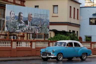 A vintage car passes by images of late Cuban President Fidel Castro, Cuba's former President Raul Castro, and Cuba's President Miguel Diaz-Canel displayed on a billboard in Havana, Cuba, May 15, 2026.