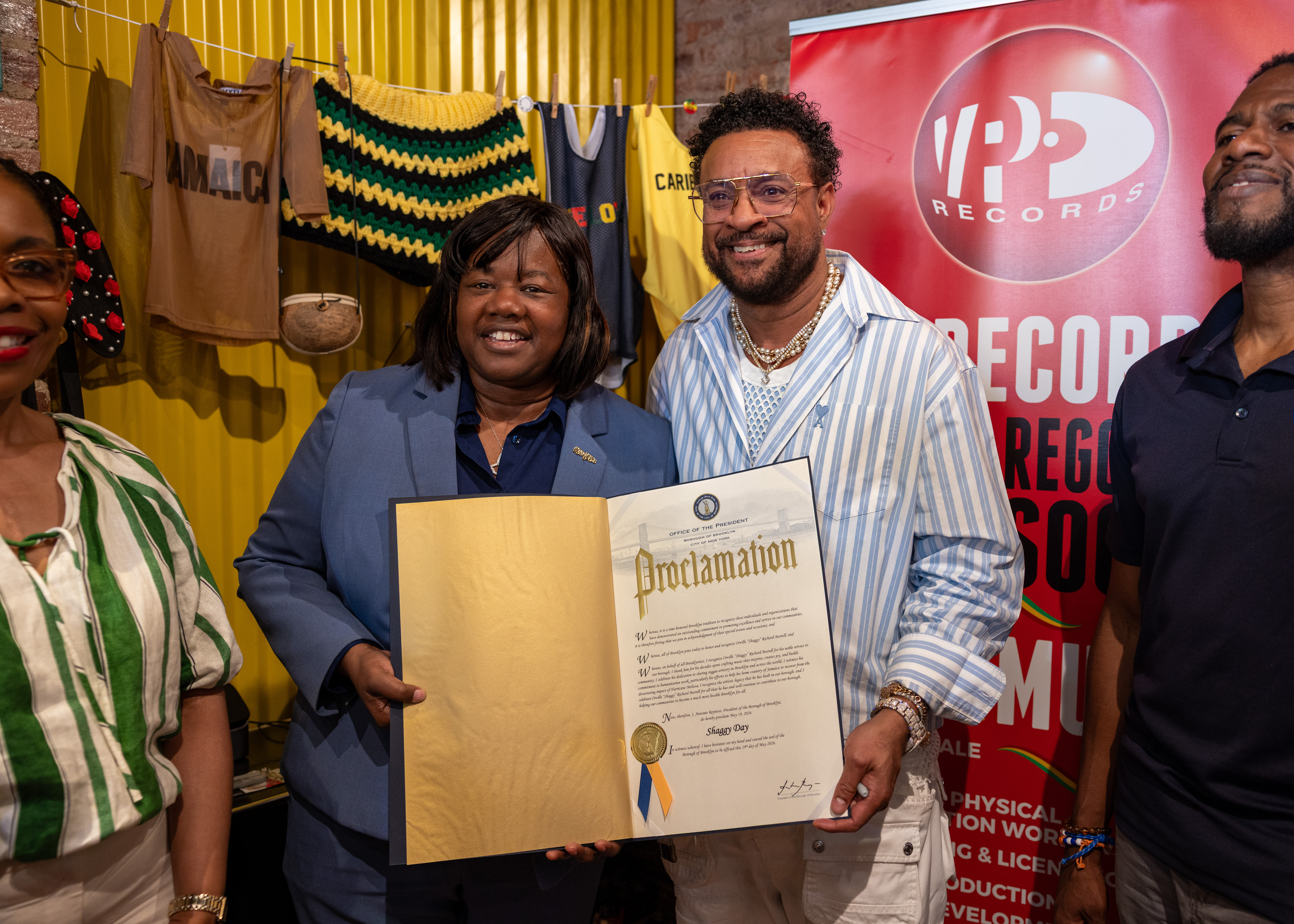 Deputy Brooklyn Borough President Kim Council, presented a Proclamation to "Hey Sexy Lady" singer Shaggy, a Grammy winner, in Little Caribbean, Brookly. Partly-hidden, left, is Council Member Rita Joseph. Partly-hidden far right, is Public Advocate Jumaane Williams. May 19, 2026 was proclaimed Shaggy Day by Brooklyn Borough President Antonio Reynoso.