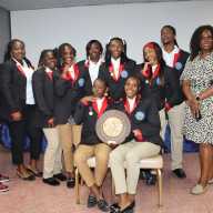 Athletes from Charles E. Mills Secondary School (CEMSS) in St. Kitts and Nevis display a plaque won at Penn Relays, flanked by management: Deputy Consul General Kressell Daniel, left; and Kylla Herbert, left, coordinator of the St. Kitts and Nevis Penn Relays initiative.