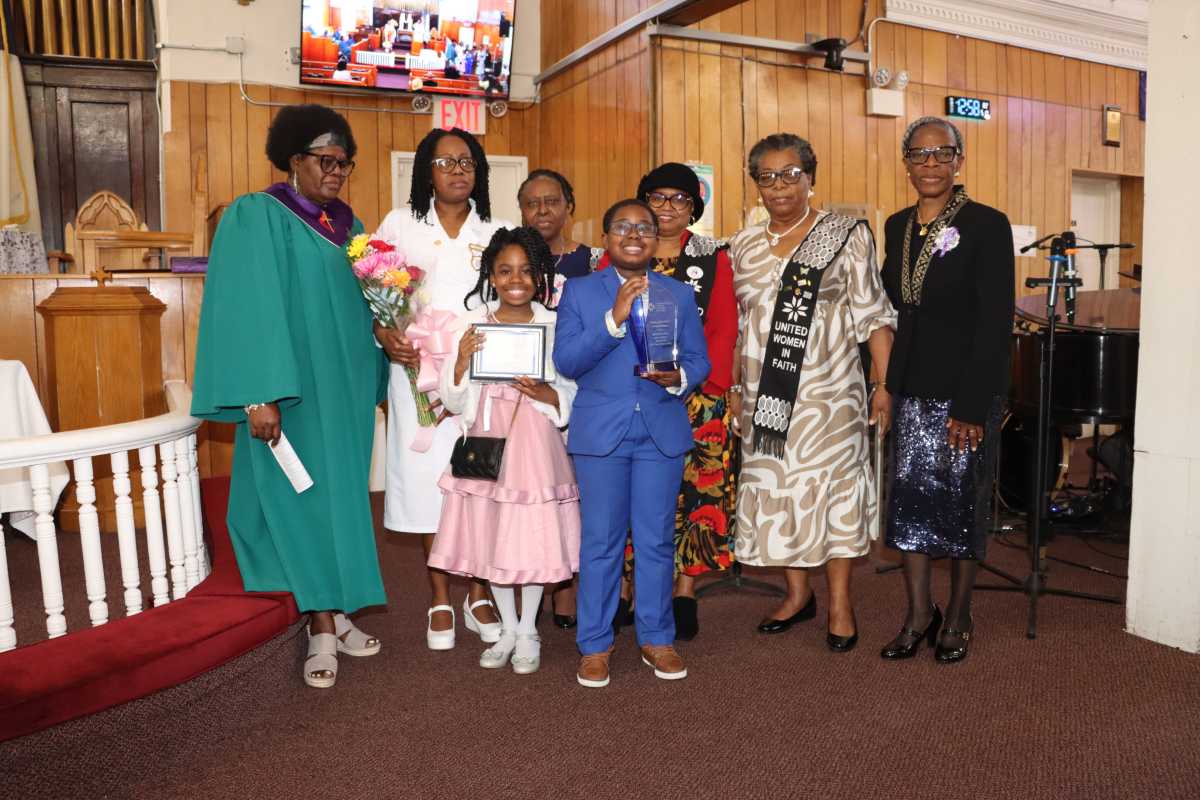 Valcia Williams's son, Nicholas Charles, holds a plaque, and daughter, Noelani Charles, holds a certificate. Valcia Williams is in a white usher dress; her mother, Catherine Williams, is left. They are flanked by members of the UWF Special Recognition Committee. UWF President Marlene Ferguson is at right.
