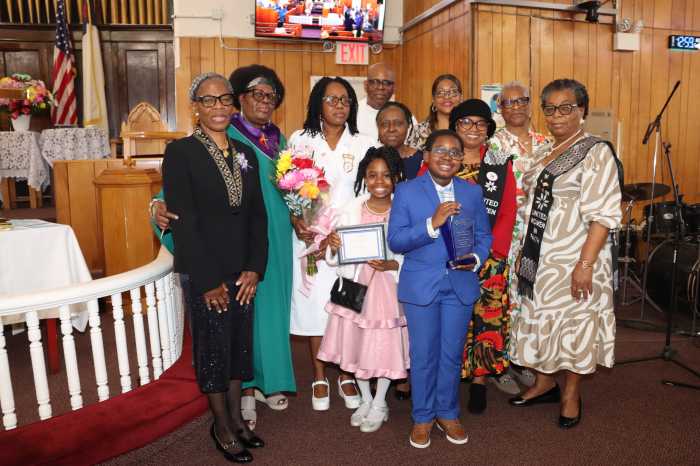 The Rev. Roger Jackson, pastor, and Sis. Kim Jackson, at back, with Valcia Williams, in a white usher dress, with flowers; her children; and members of the United Women in Faith (UWF).